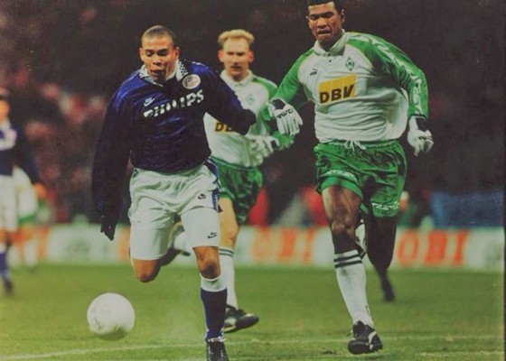 Com luvas de goleiro pelo Bremen, Júnior Baiano (à dir.) disputa corrida com Ronaldo pelo PSV, em 1995 na Alemanha